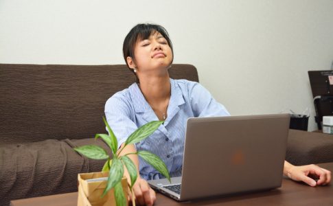 ノートパソコンの前で目をつぶる女性